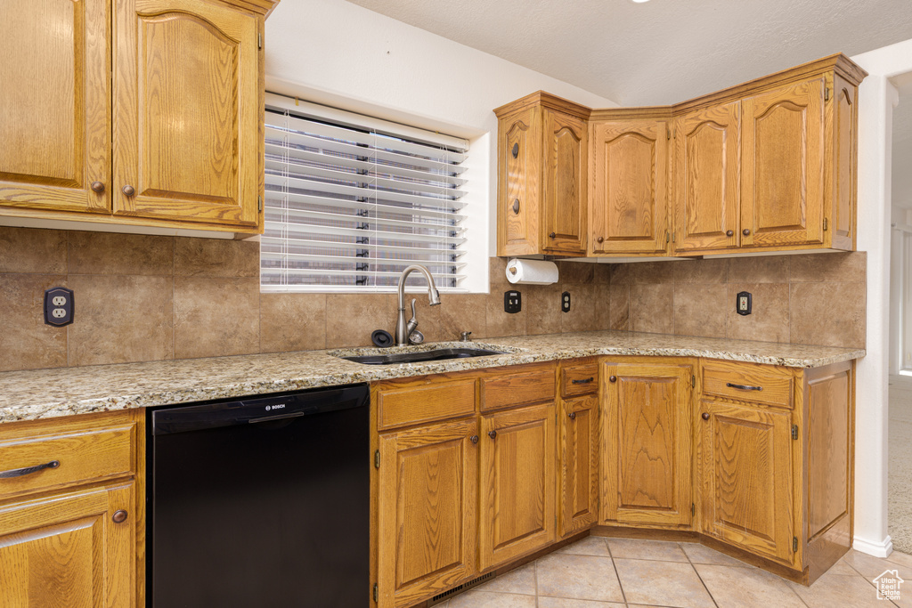 Kitchen featuring black dishwasher, a sink, tasteful backsplash, light tile patterned flooring, and light stone counters