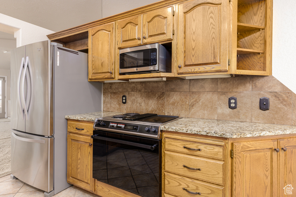 Kitchen with appliances with stainless steel finishes, backsplash, light stone countertops, and light tile patterned floors