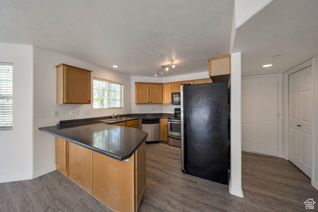 Kitchen with a peninsula, a textured ceiling, dark wood-style flooring, dark countertops, and black appliances