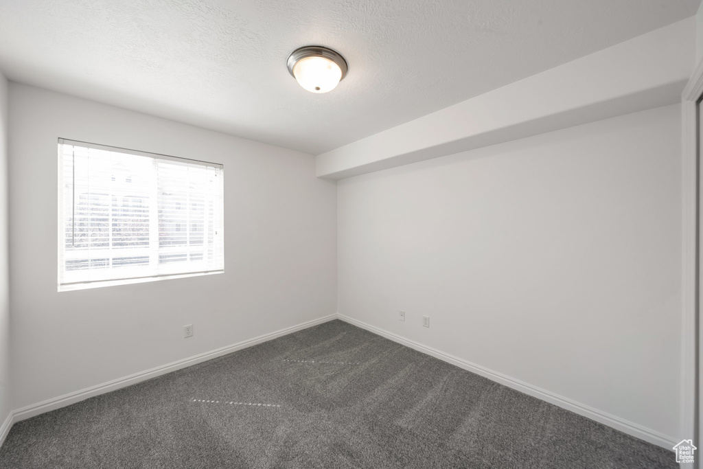 Spare room featuring dark colored carpet and baseboards