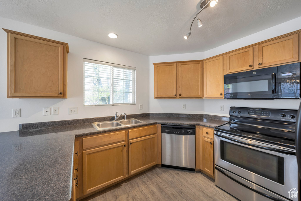 Kitchen with dark countertops, a sink, brown cabinets, light wood-type flooring, and stainless steel appliances