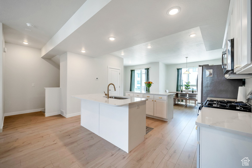 Kitchen featuring a sink, a center island with sink, stainless steel microwave, light wood finished floors, and recessed lighting