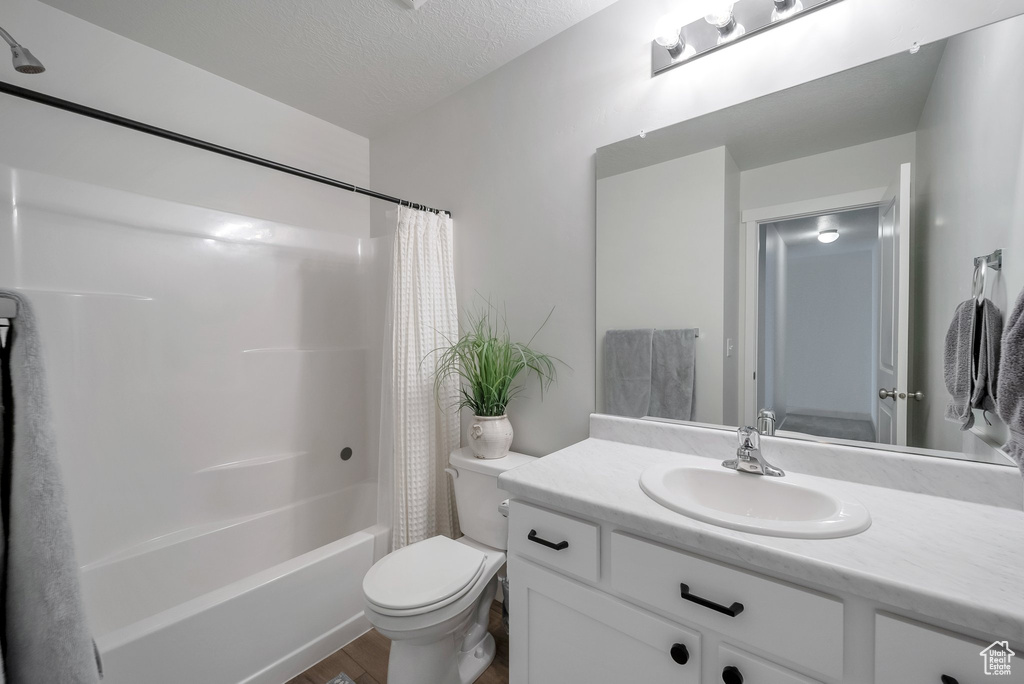 Bathroom featuring wood finished floors, a textured ceiling, toilet, vanity, and shower / tub combo with curtain