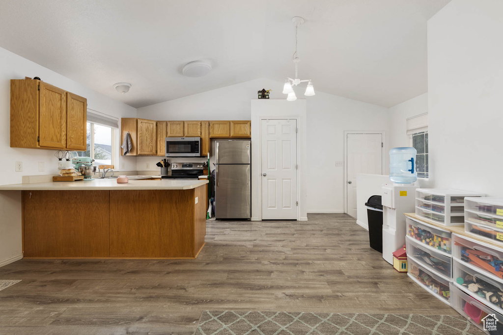 Kitchen featuring appliances with stainless steel finishes, a peninsula, lofted ceiling, wood finished floors, and light countertops