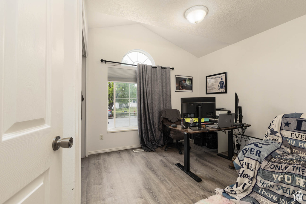 Home office featuring wood finished floors, lofted ceiling, and a textured ceiling