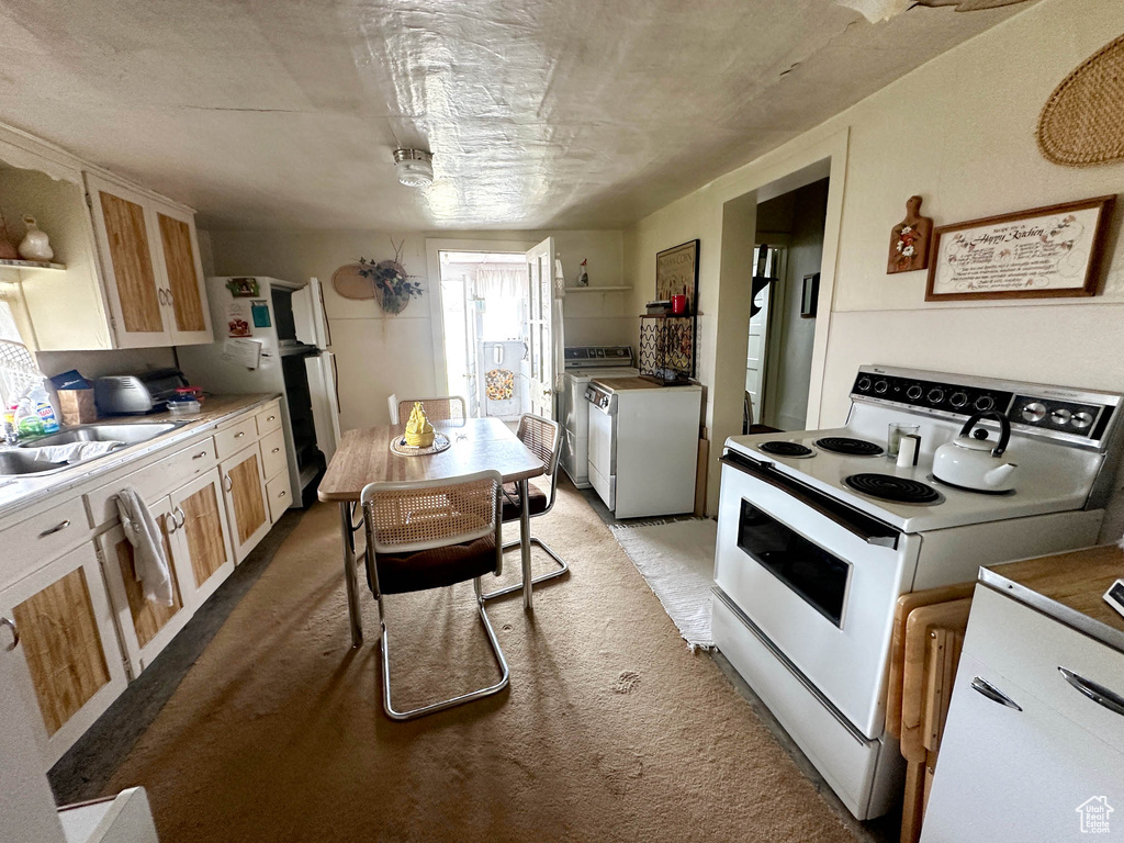Kitchen with white electric stove, carpet floors, a sink, and independent washer and dryer