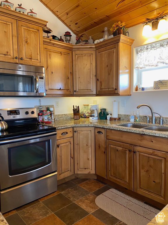 Kitchen featuring appliances with stainless steel finishes, lofted ceiling, a sink, wood ceiling, and dark stone finish floors