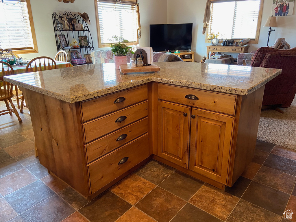 Kitchen with stone tile floors, plenty of natural light, brown cabinetry, and light stone counters