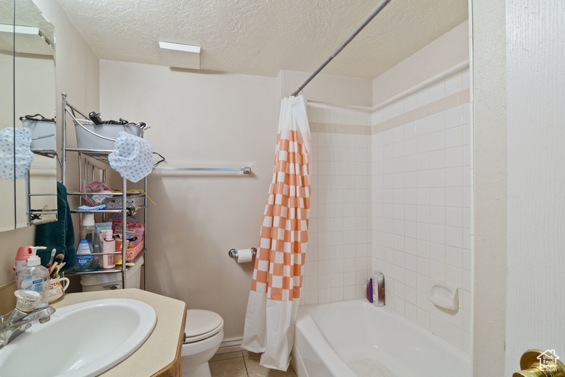 Bathroom with toilet, tile patterned floors, shower / bath combination with curtain, a textured ceiling, and vanity