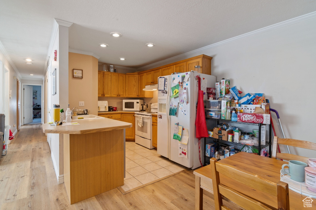 Kitchen with white appliances, crown molding, a peninsula, a sink, and light countertops
