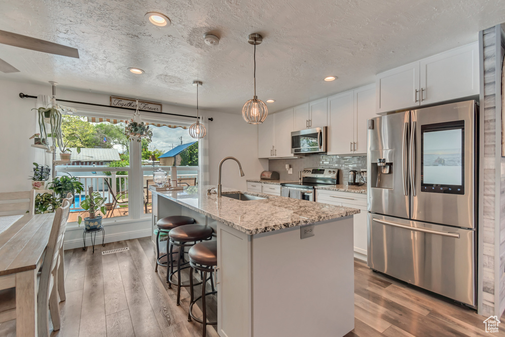 Kitchen featuring stainless steel appliances, a sink, wood finished floors, white cabinets, and a textured ceiling