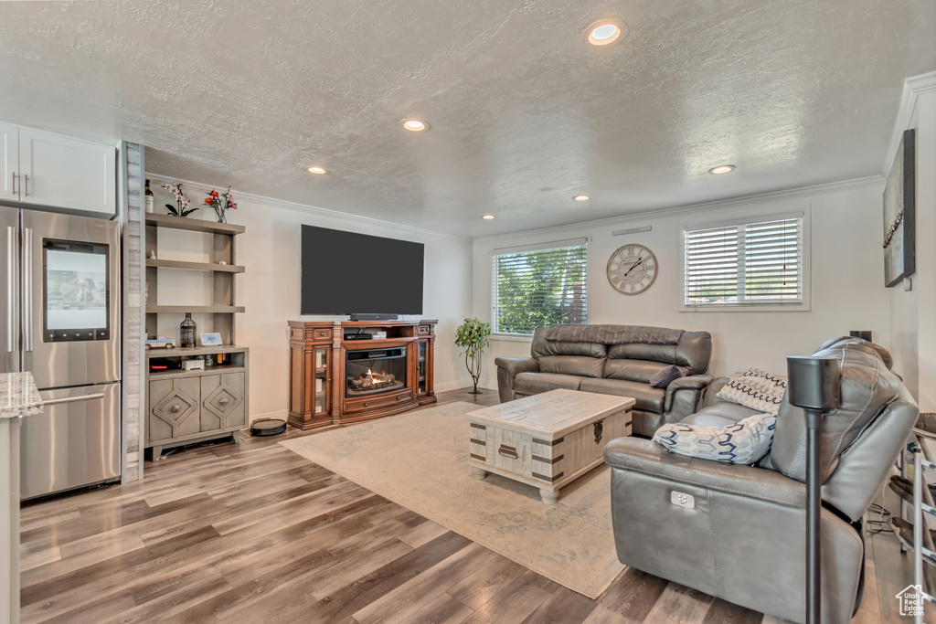 Living room featuring crown molding, light wood-style floors, a textured ceiling, a glass covered fireplace, and recessed lighting
