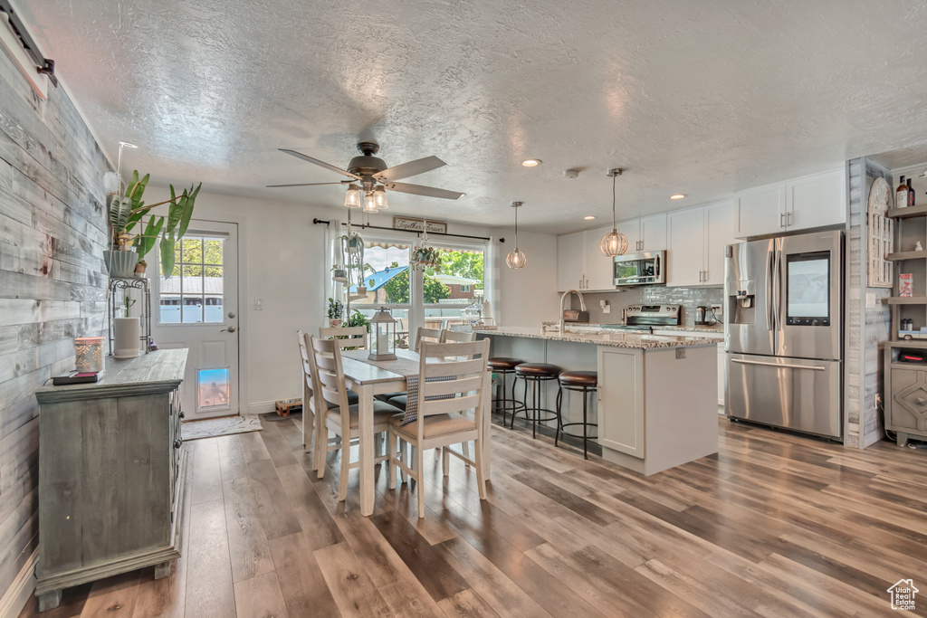 Dining area with plenty of natural light, ceiling fan, wood finished floors, a textured ceiling, and baseboards
