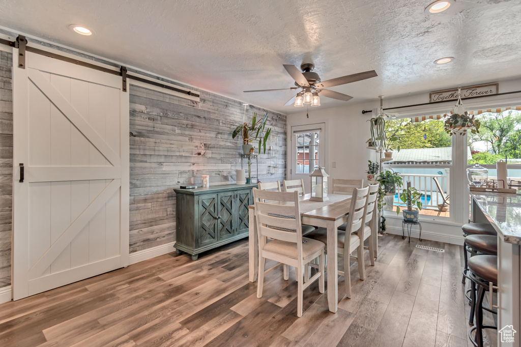 Dining area featuring a barn door, baseboards, ceiling fan, wood finished floors, and a textured ceiling