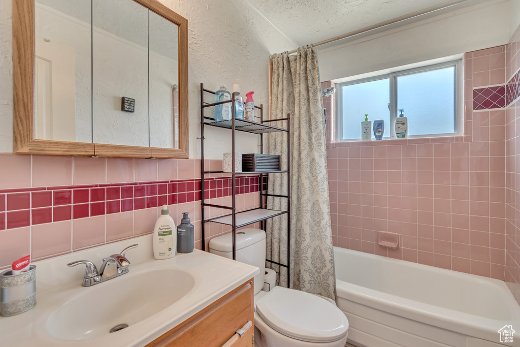 Bathroom featuring toilet, shower / bathtub combination with curtain, vanity, and tile walls