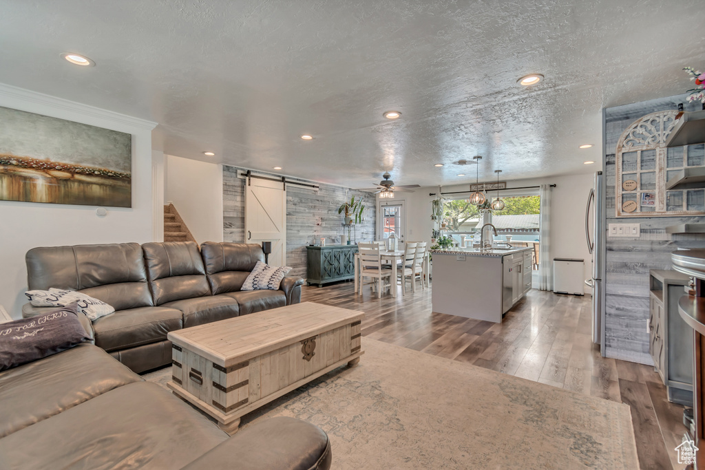 Living area with a barn door, light wood-style floors, recessed lighting, a textured ceiling, and a ceiling fan