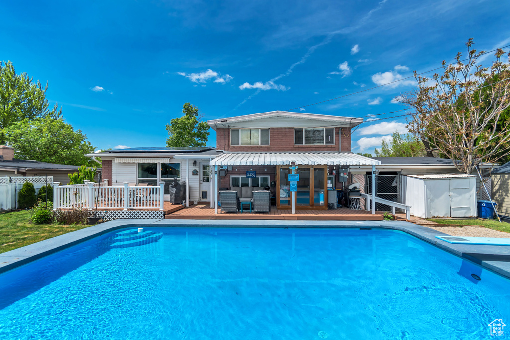 View of swimming pool with a wooden deck, an outbuilding, a storage shed, and fence