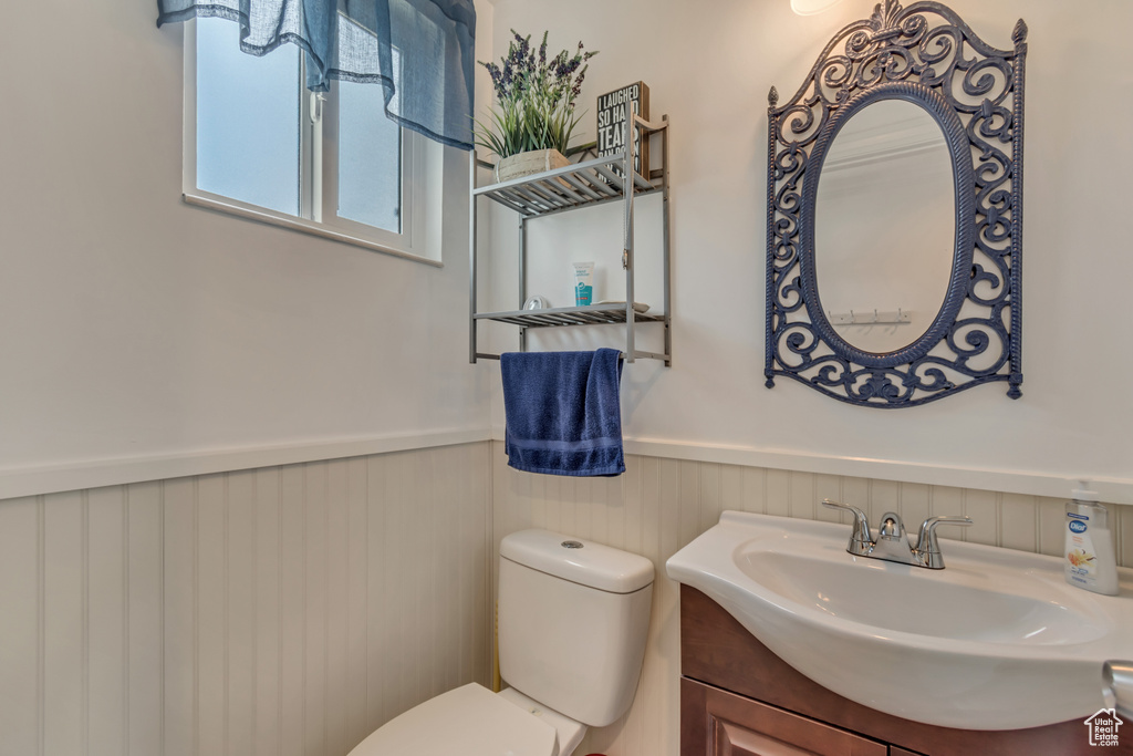 Half bath with a wainscoted wall, toilet, and vanity