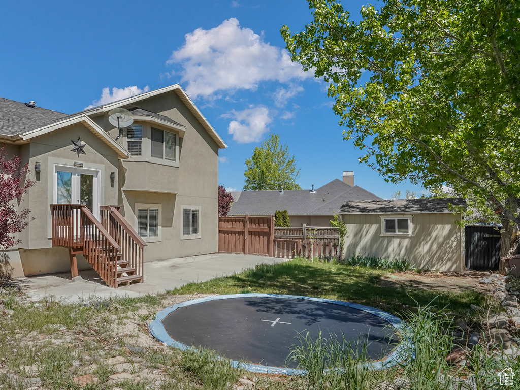 Back of house with a trampoline, a fenced backyard, stucco siding, and a patio area