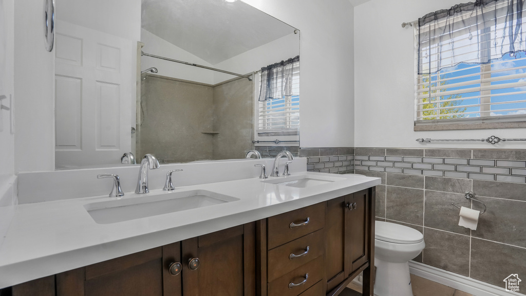 Bathroom featuring toilet, tile walls, double vanity, tile patterned flooring, and wainscoting