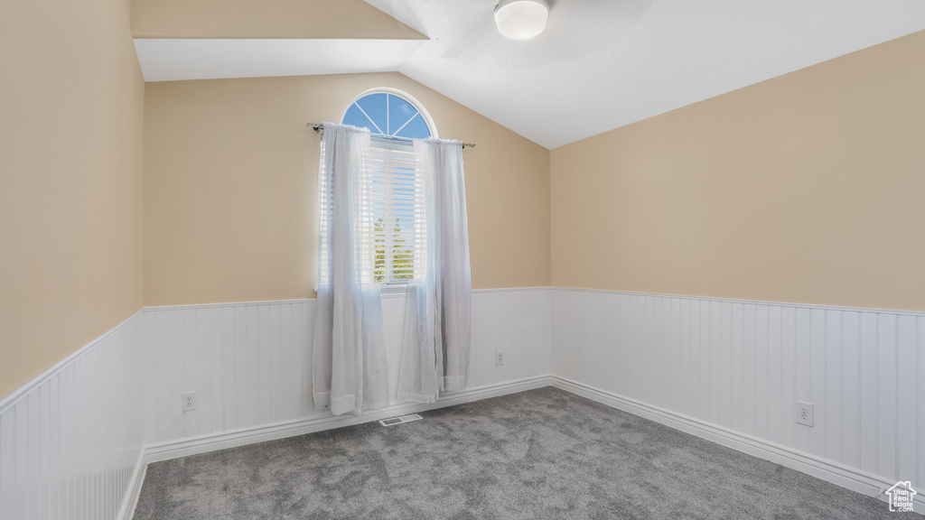 Carpeted empty room with a wainscoted wall, lofted ceiling, healthy amount of natural light, and ceiling fan