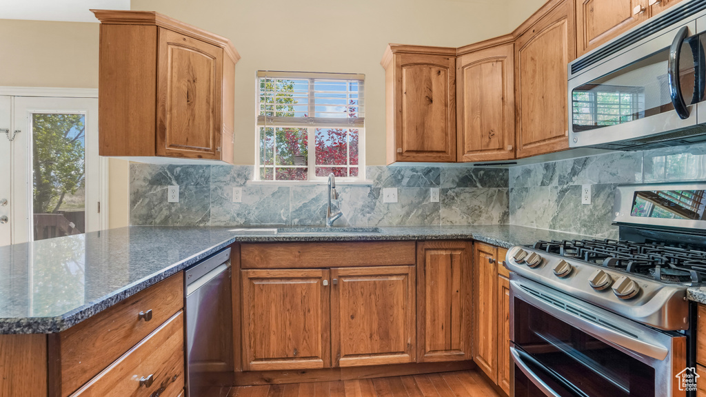 Kitchen featuring appliances with stainless steel finishes, a sink, dark stone countertops, and decorative backsplash