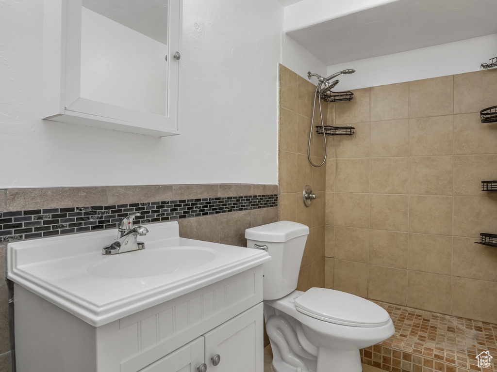 Full bathroom featuring toilet, tiled shower, vanity, tile walls, and a wainscoted wall