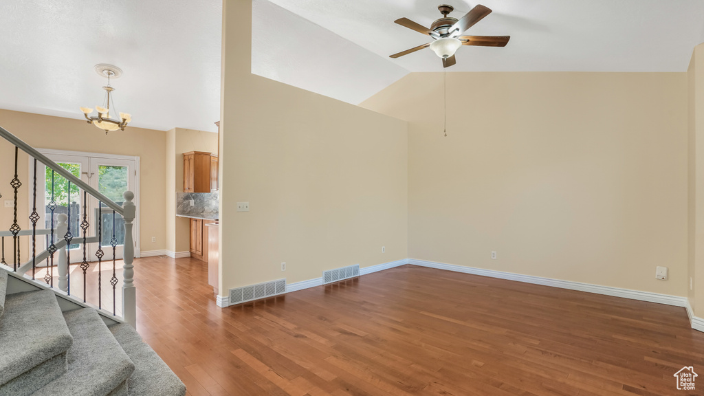 Empty room featuring stairway, ceiling fan, a chandelier, wood finished floors, and vaulted ceiling
