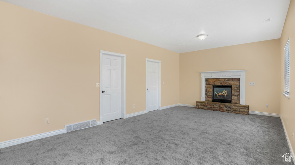 Unfurnished living room featuring carpet, a stone fireplace, and baseboards