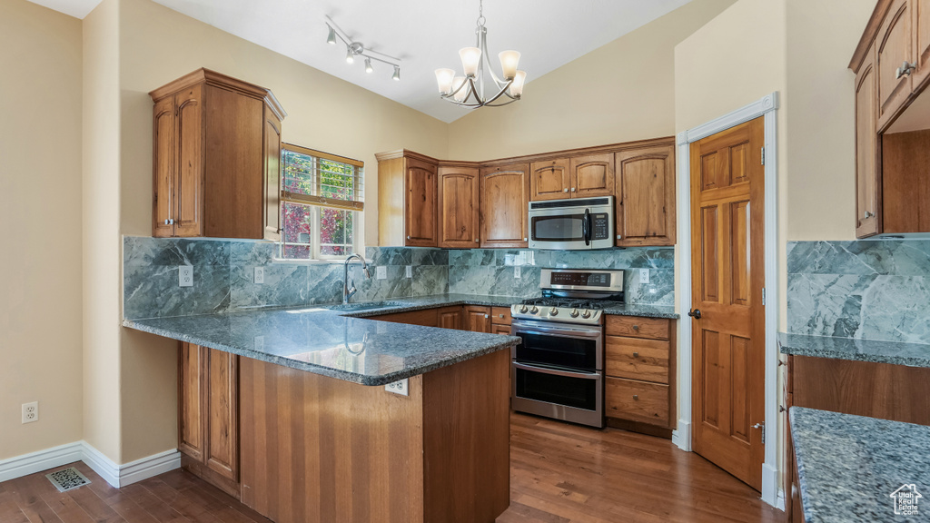Kitchen featuring stainless steel appliances, a sink, a chandelier, a peninsula, and dark wood-type flooring