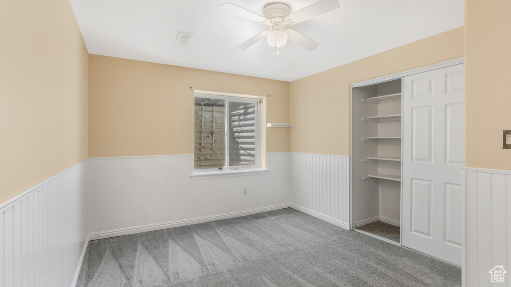 Carpeted empty room featuring wainscoting and a ceiling fan