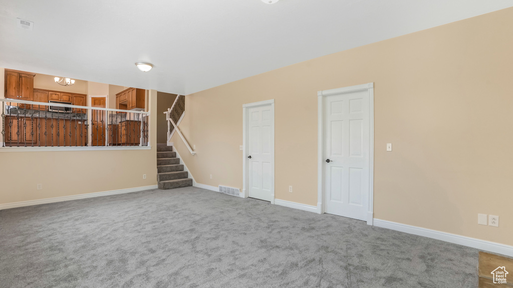 Unfurnished living room featuring light colored carpet, stairway, and baseboards