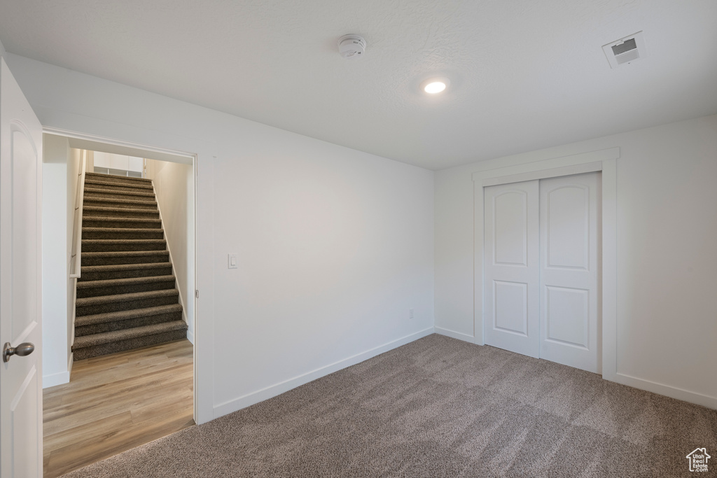 Empty room with a smoke detector, light carpet, stairway, and baseboards