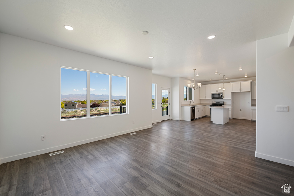 Unfurnished living room with a chandelier, recessed lighting, baseboards, dark wood-style flooring, and a sink