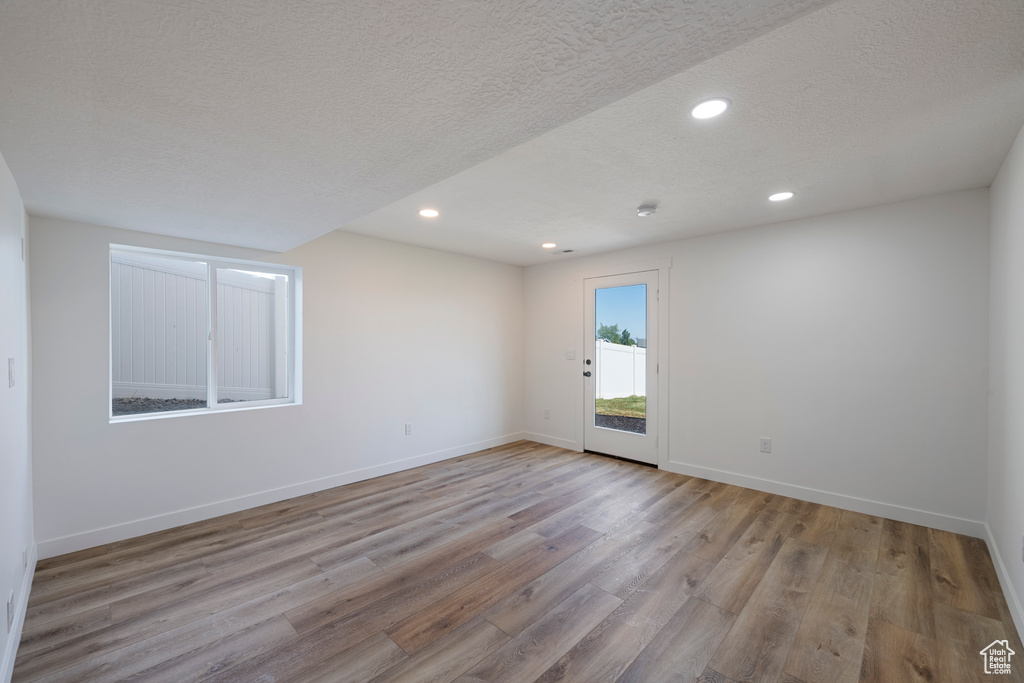 Empty room featuring wood finished floors, a textured ceiling, recessed lighting, and baseboards
