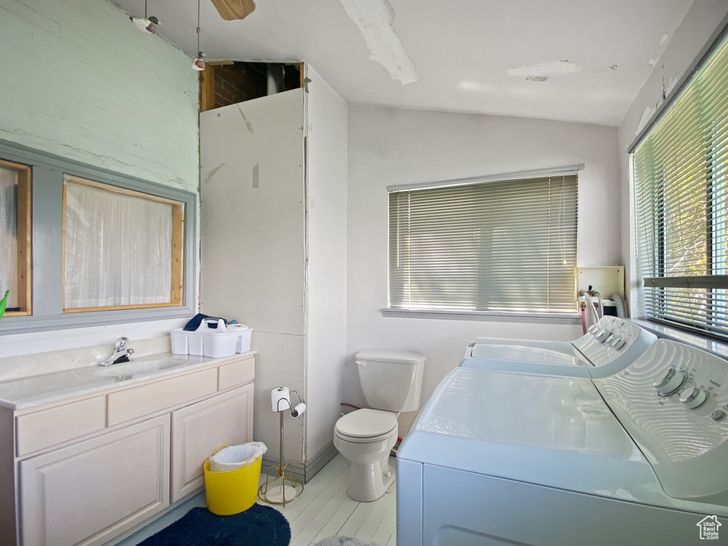Bathroom with independent washer and dryer, lofted ceiling, vanity, toilet, and wood finished floors