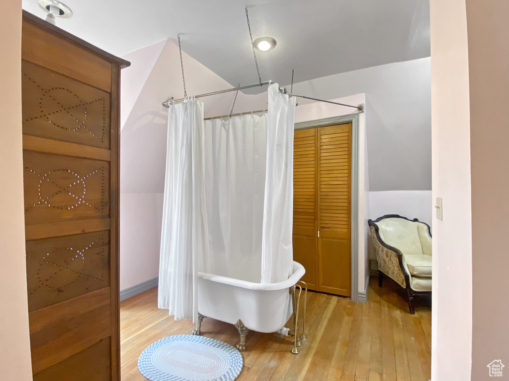 Bathroom with wood-type flooring, a freestanding bath, and curtained shower