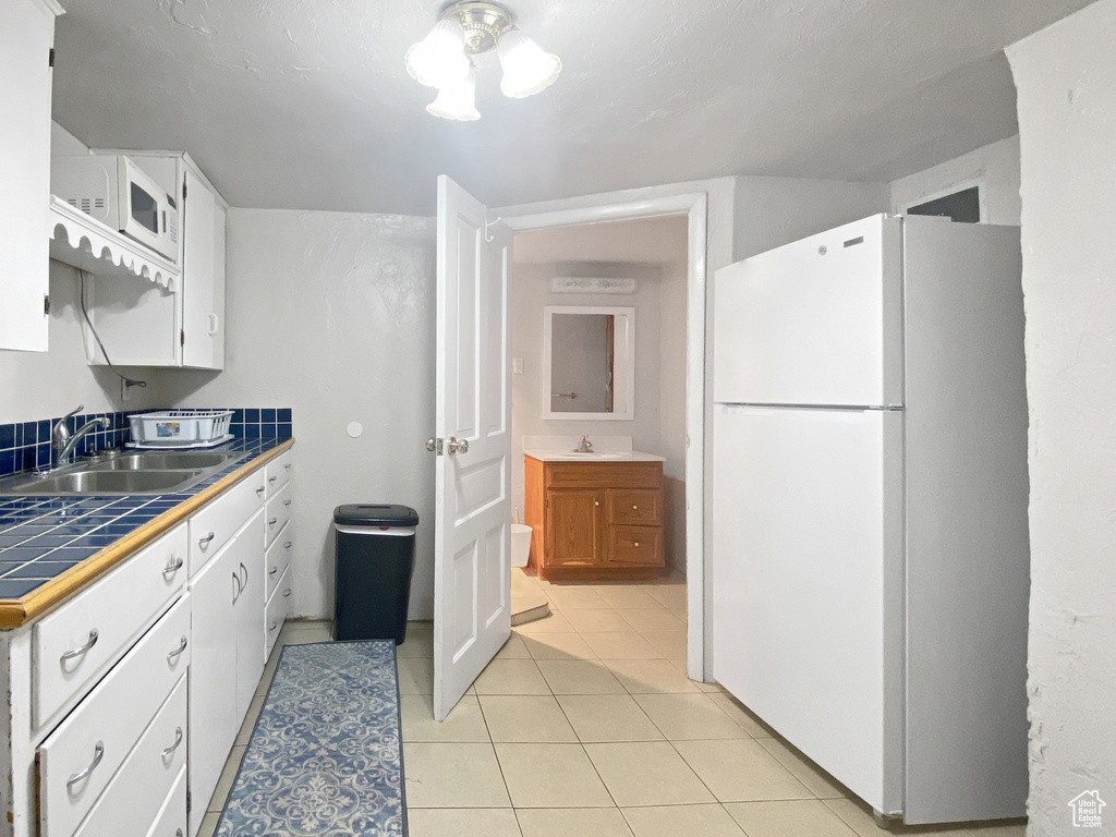 Kitchen featuring freestanding refrigerator, tile counters, a sink, and white cabinets