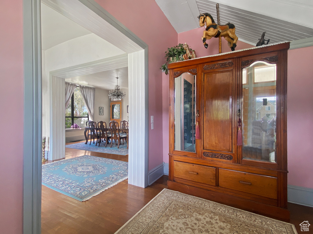 Entrance foyer with a chandelier, wood finished floors, baseboards, and vaulted ceiling