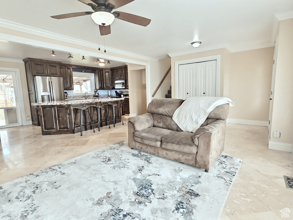 Living room with crown molding, ceiling fan, baseboards, and stairs