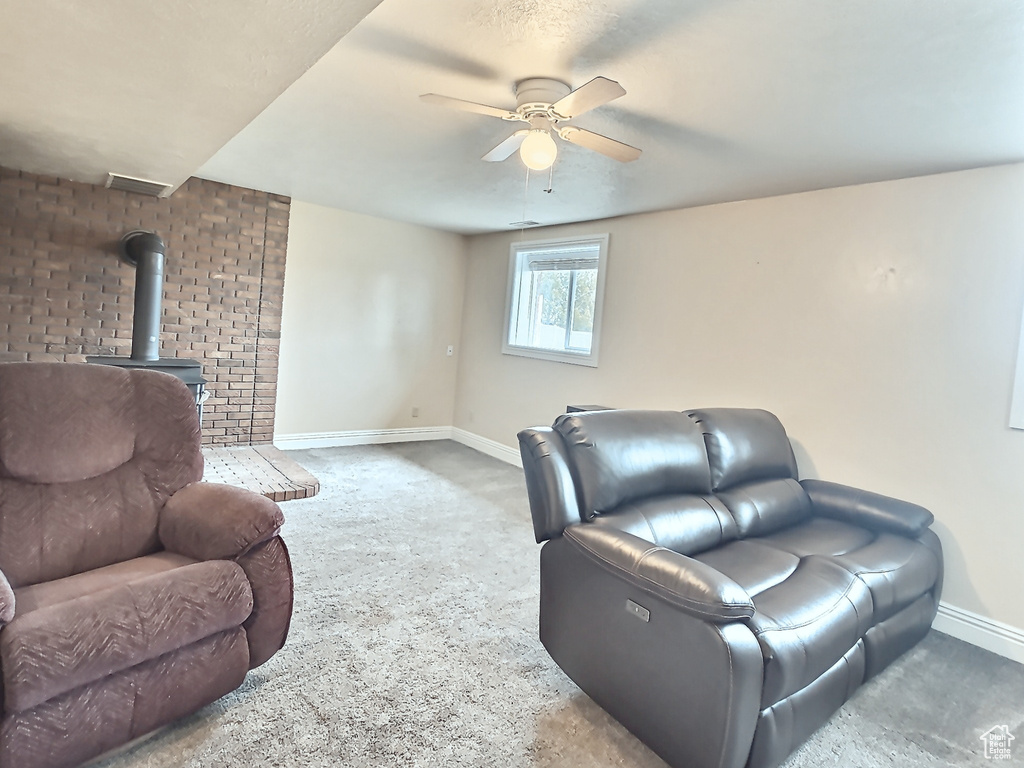 Carpeted living room featuring a wood stove, baseboards, and a ceiling fan
