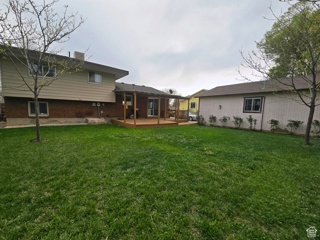 Back of property featuring a deck, a lawn, and brick siding