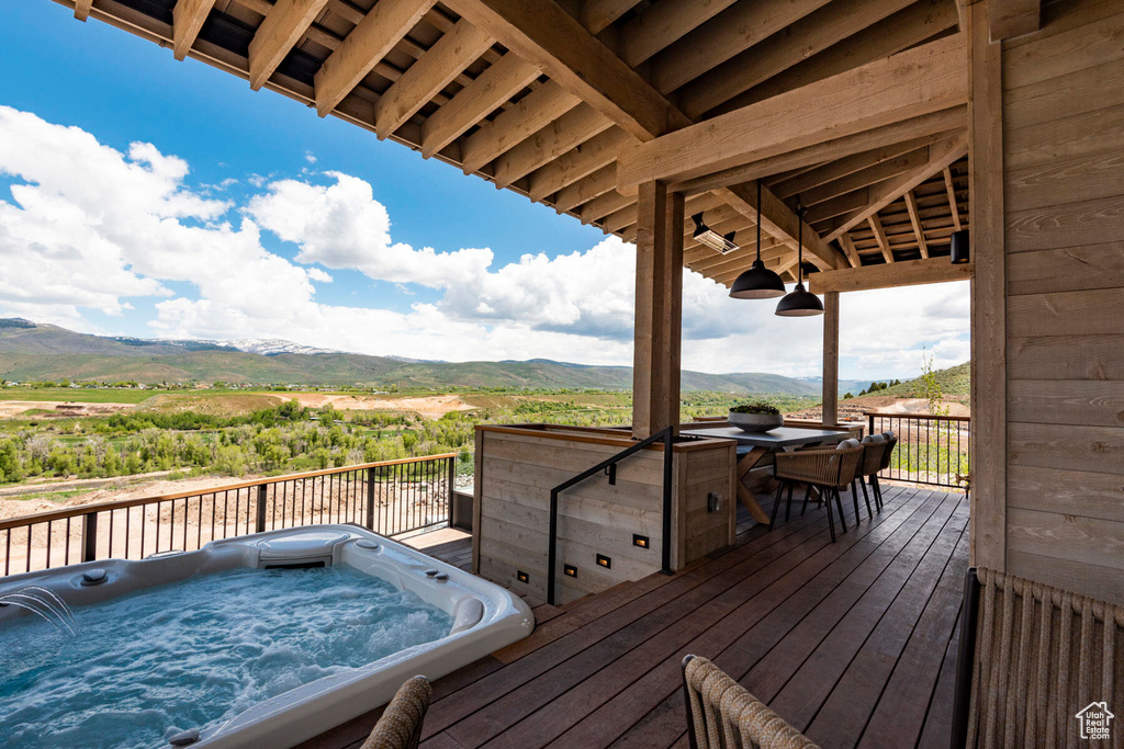 Wooden terrace featuring a mountain view, an outdoor hot tub, and outdoor dining area