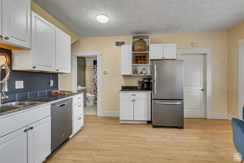 Kitchen with appliances with stainless steel finishes, white cabinetry, a sink, dark countertops, and open shelves