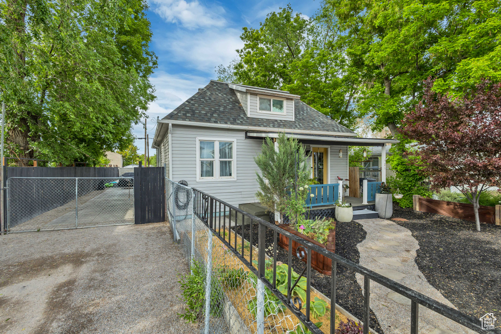 Bungalow-style house featuring a shingled roof, a porch, fence, and a gate
