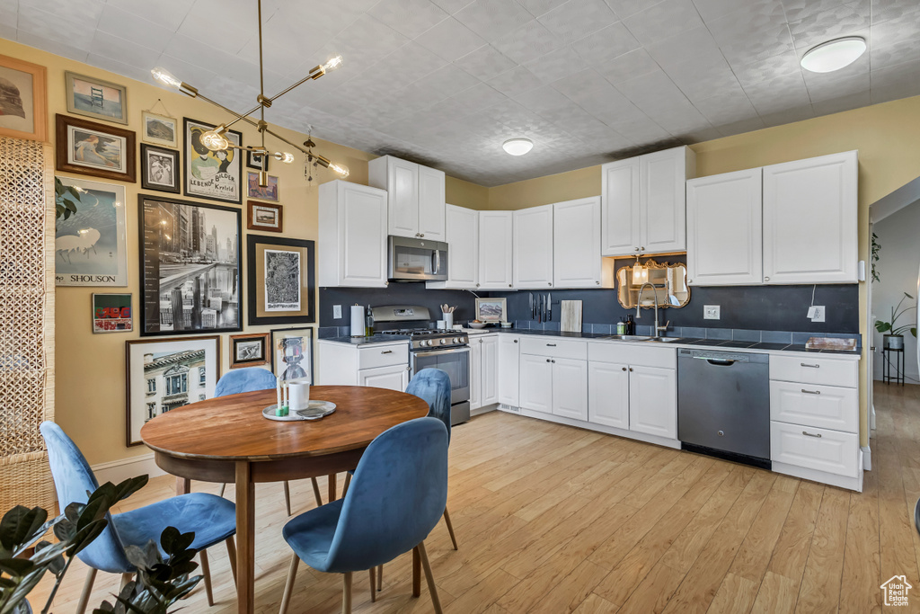 Kitchen featuring stainless steel appliances, white cabinets, light wood-style flooring, and dark countertops