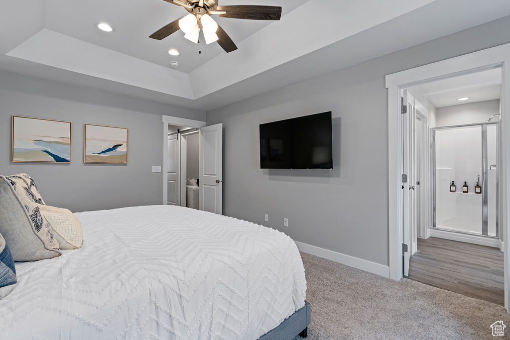 Carpeted bedroom featuring a tray ceiling, recessed lighting, baseboards, ensuite bath, and a ceiling fan