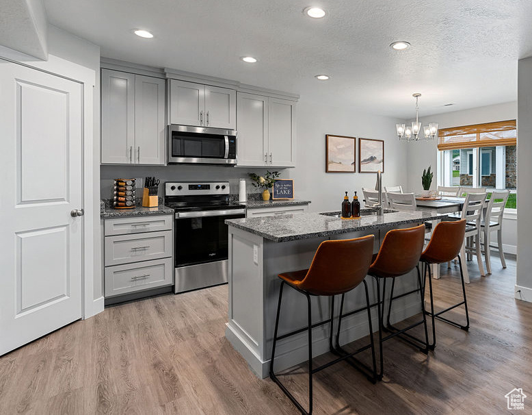 Kitchen with appliances with stainless steel finishes, dark stone countertops, a kitchen island with sink, a kitchen breakfast bar, and a chandelier