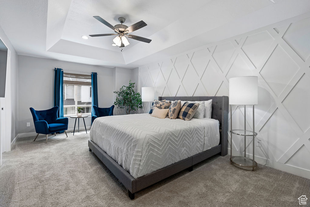 Carpeted bedroom with a raised ceiling, a ceiling fan, and baseboards