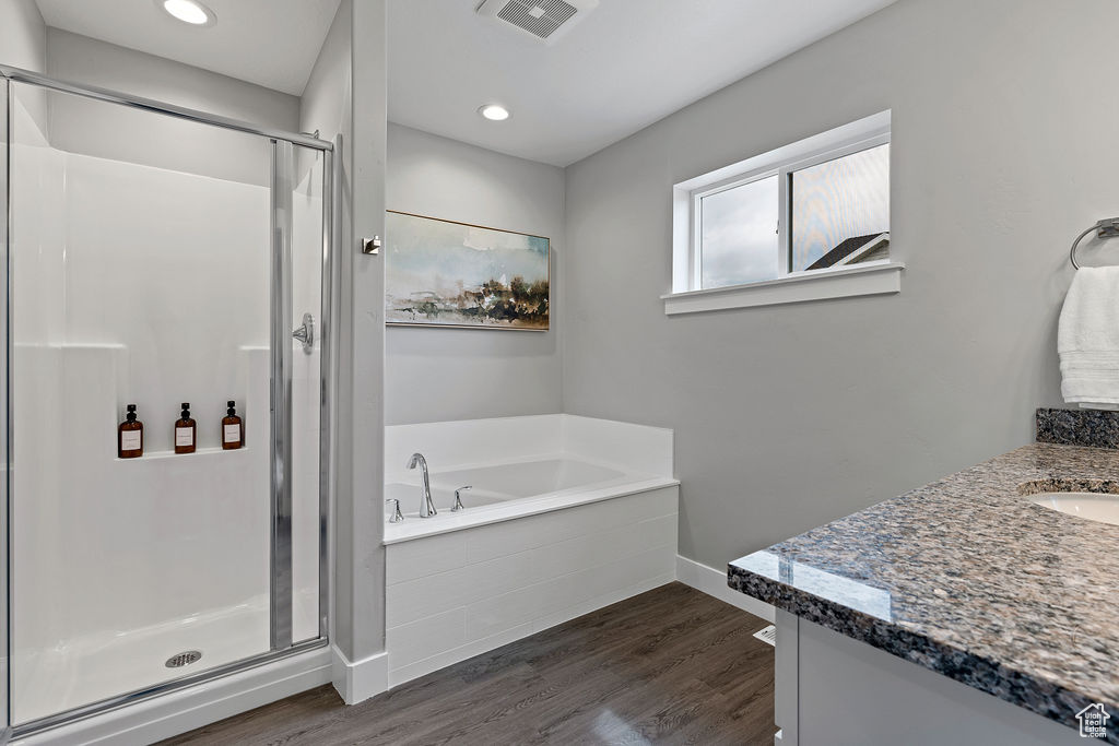 Bathroom with a stall shower, a garden tub, wood finished floors, vanity, and baseboards